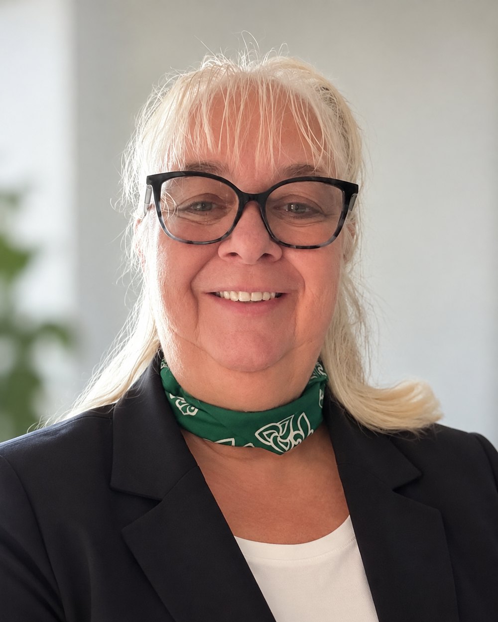 Angèle Lacroix, souriante, cheveux blonds longs, lunettes à monture foncée, veston marine et foulard vert et blanc.